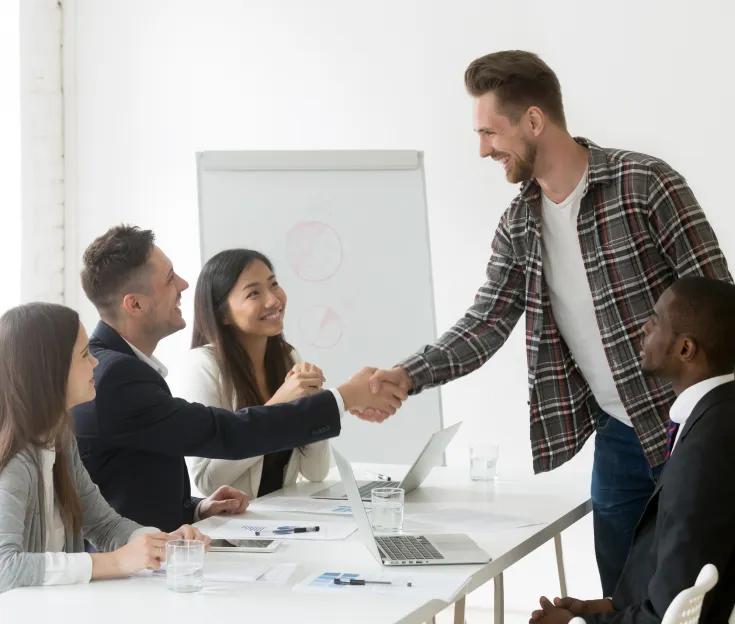 A smiling young man greeting people in a meeting with a handshake